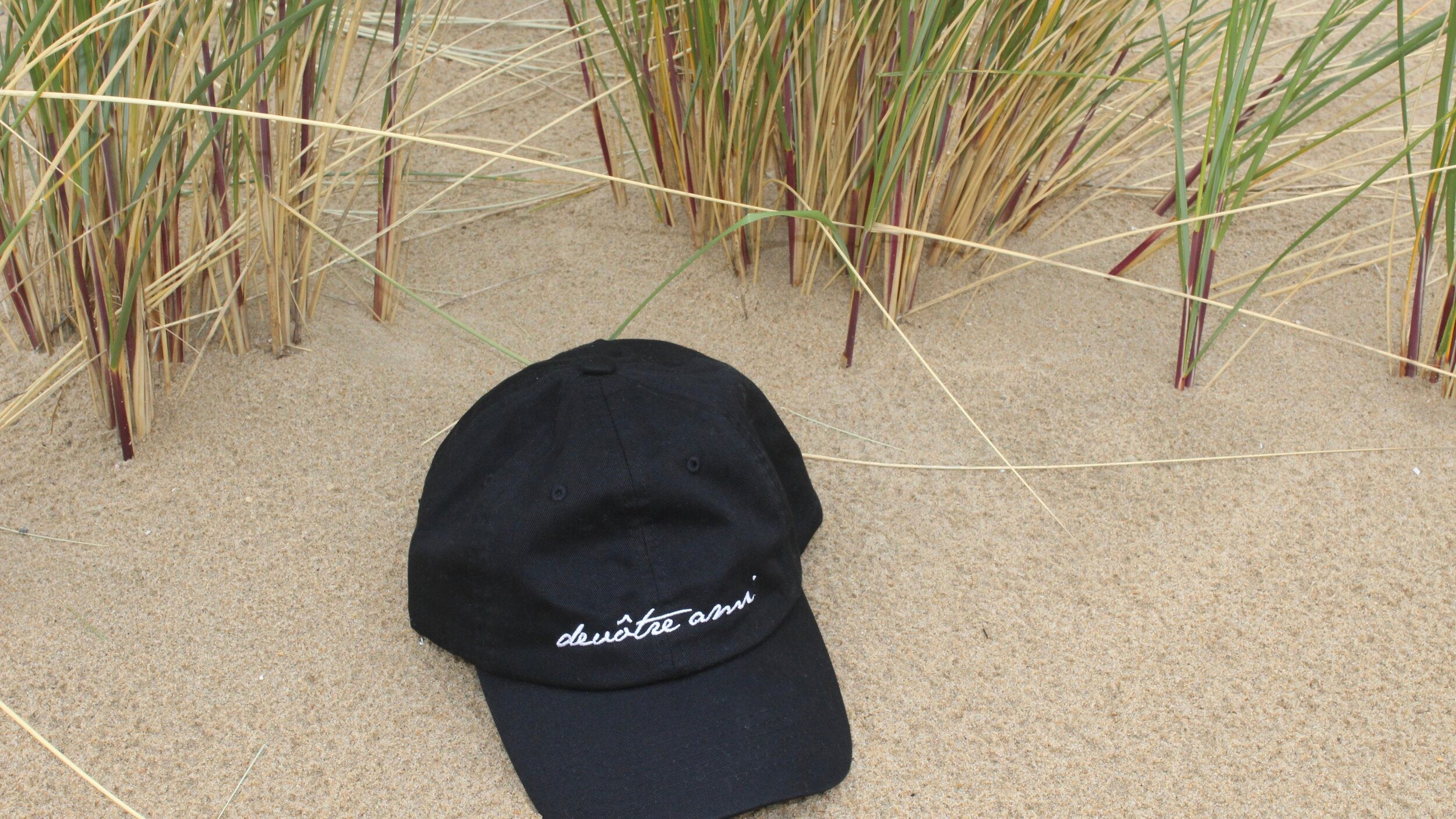 A black branded cap on a sandy background, showcasing the Soulful Snacking lifestyle accessories baseball cap hat devôtre devotre ami logo